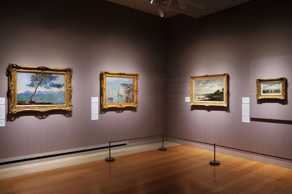 第四章「クールベと同時代の海」展示風景。左の壁の作品はクロード・モネで左が《アンティーブ岬》1888年、右が《アヴァルの門》1886年。右の壁の作品はモネの師匠であるウジェーヌ・ブーダンの作品で、左が《ブレスト、停泊地》1872年、右が《浜辺にて》。クールベはブーダンと連れ立って戸外に制作に出たり、モネを大切な年下の友人として付き合いがあり、お互いに刺激を受け合う仲であった。