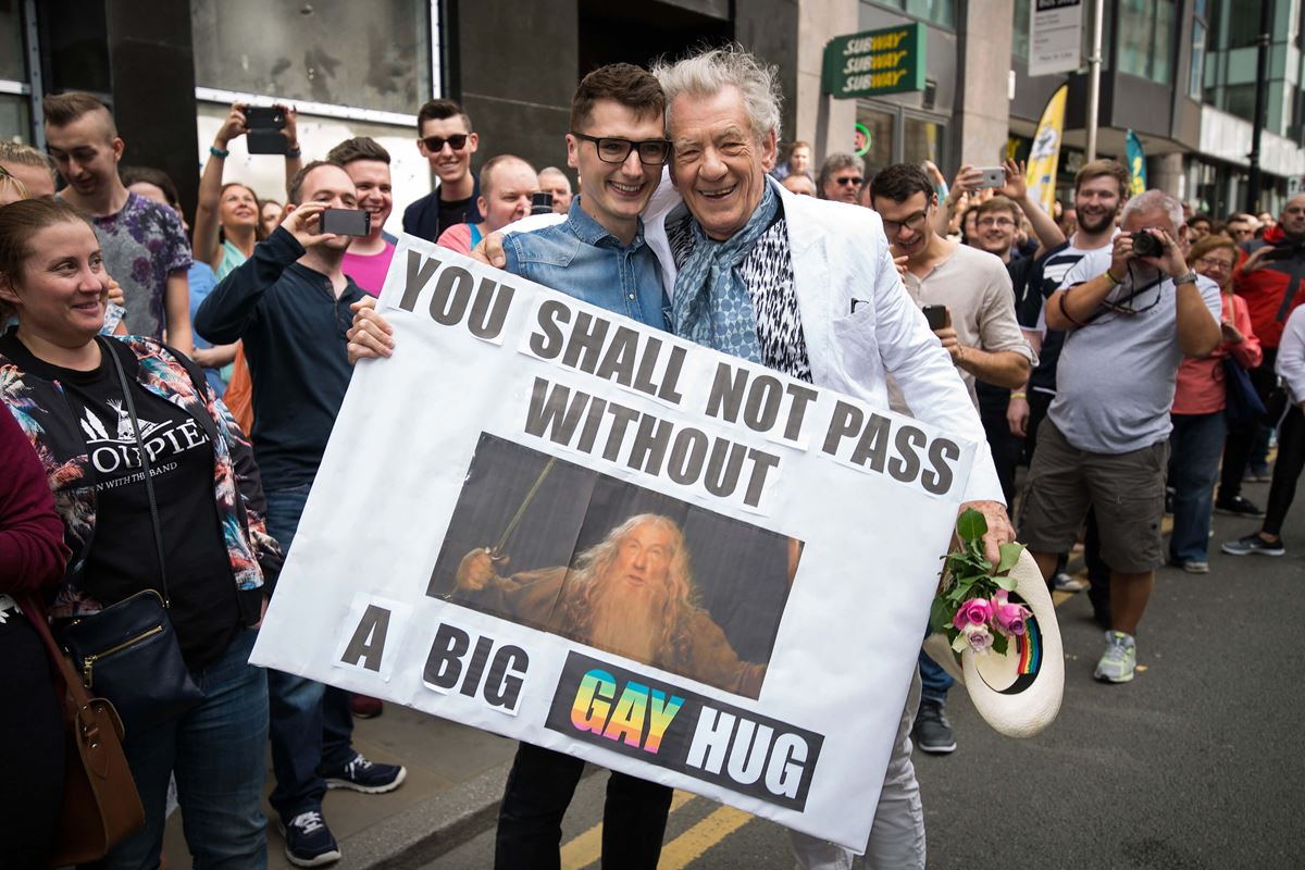 2015年、英国マンチェスターでのプライド・パレード（LGBTを讃えるイベント）で。プラカードの文章は直訳すると、“あなたはゲイの大きな抱擁なしでは通り抜けられません”。